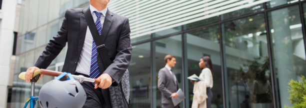 Man bikes to work with other professionals behind him in front of office building. 