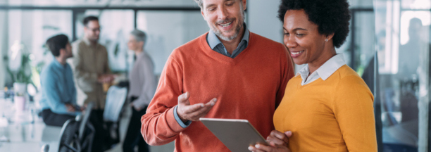 Man and woman looking at tablet in office smiling. 