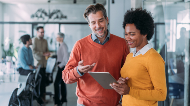Man and woman looking at tablet in office smiling. 