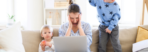 Stressed mom sitting on couch with two kids and an open laptop.