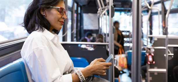 Middle aged woman commuting on a bus while looking down at her phone.